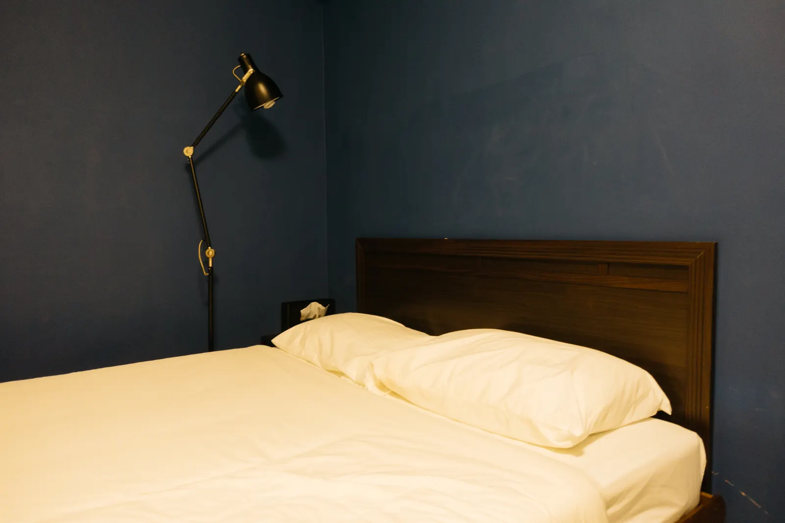 A dim bedroom with navy walls and white bedding.