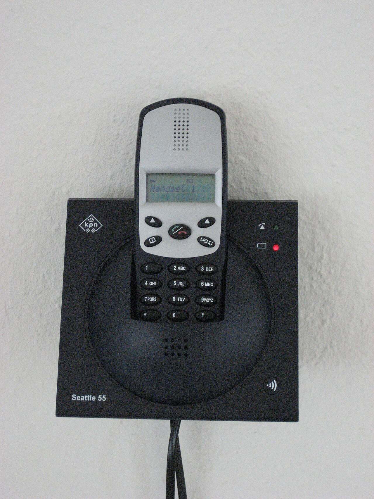A cordless telephone handset docked in its wall-mounted base.
