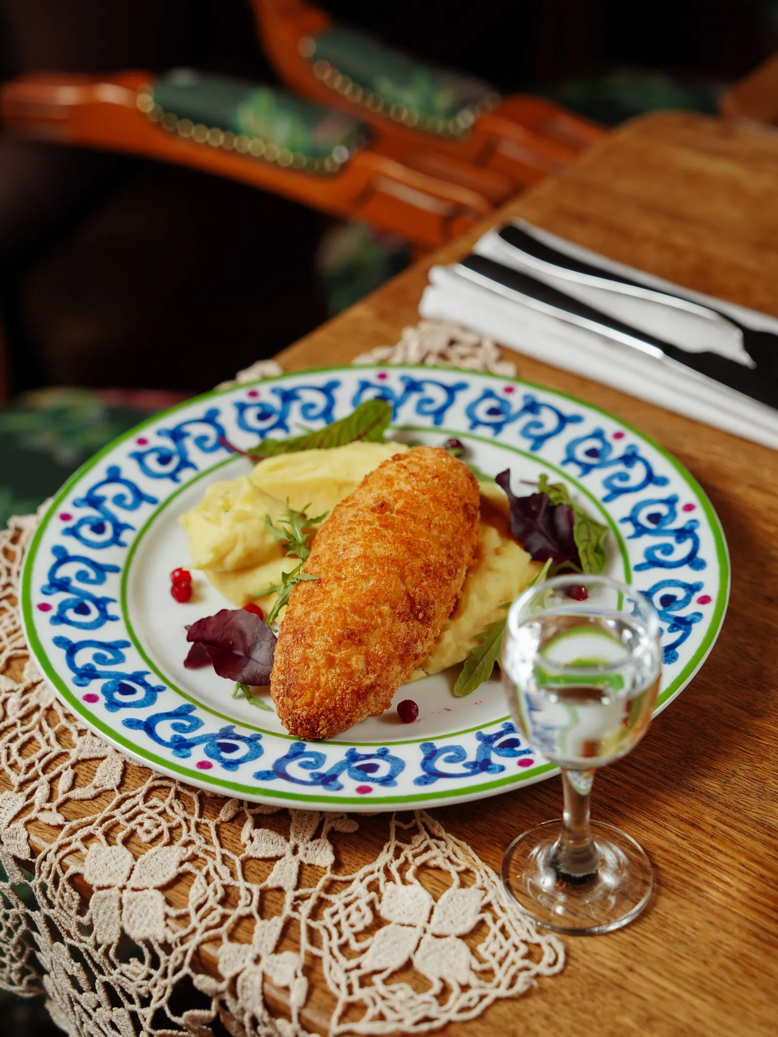 A breaded cutlet with mashed potato and salad on a painted plate.