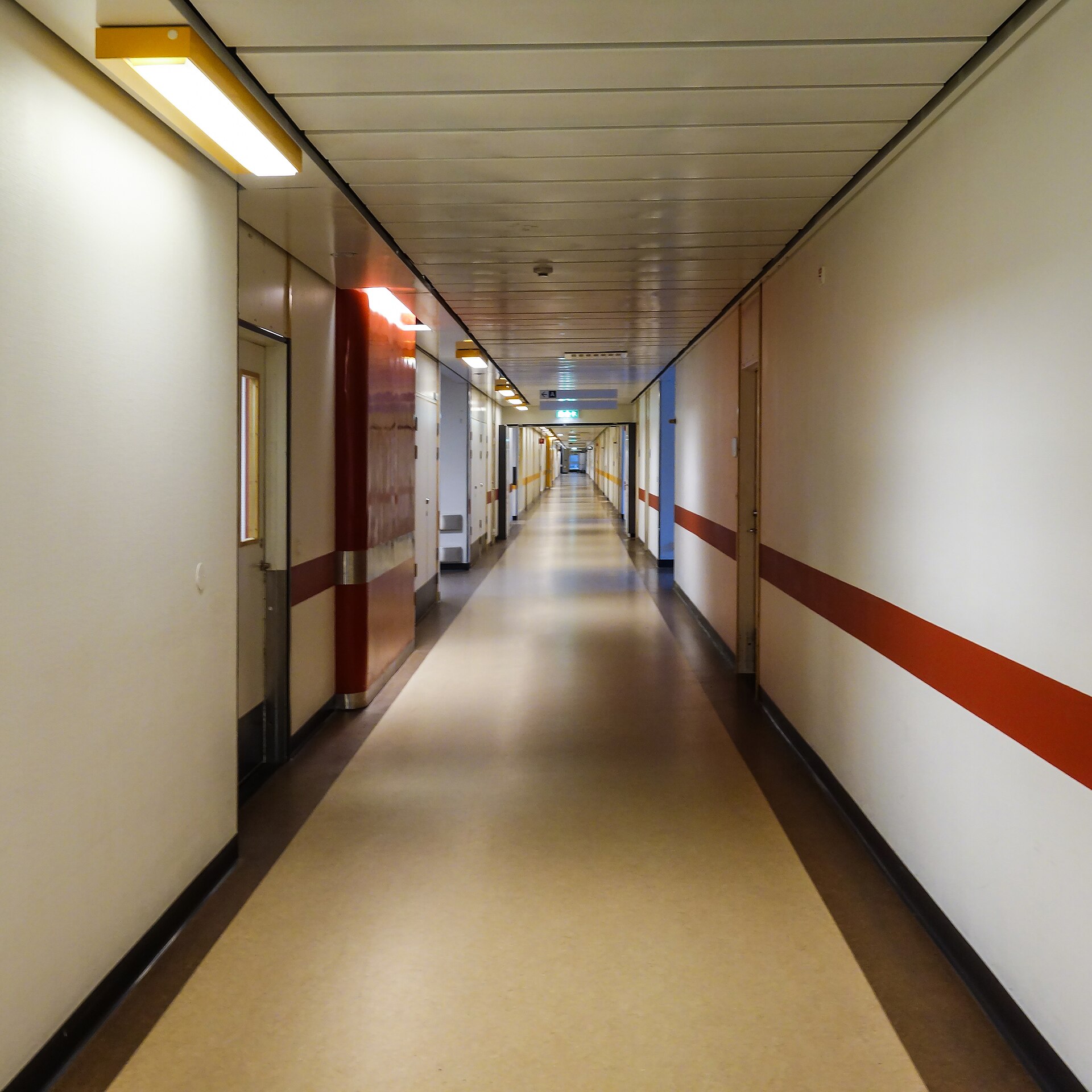 A long, empty hospital corridor with cream walls and a red stripe.