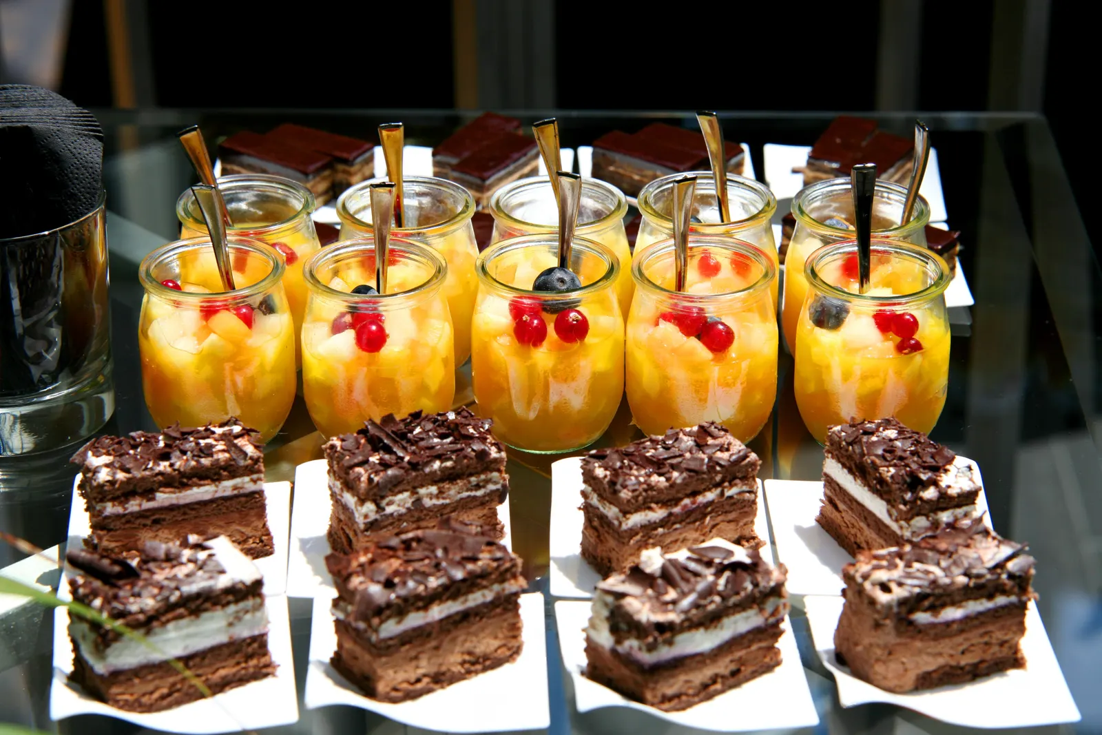 Small jars of fruit jelly with spoons, in front of slices of chocolate cake.