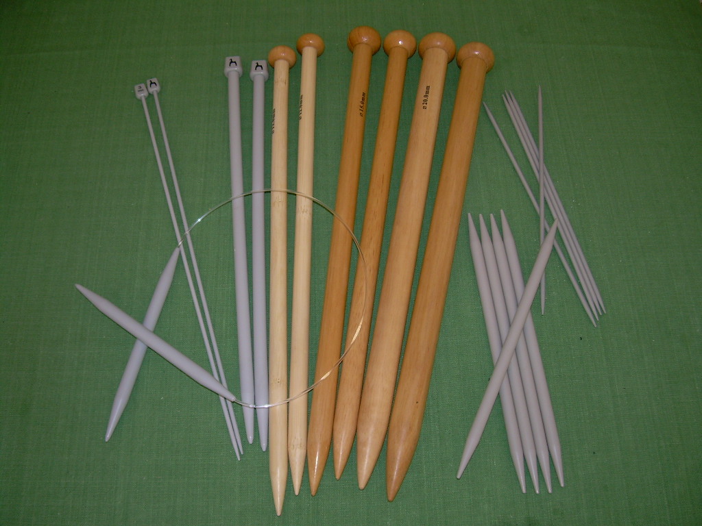 Knitting needles of several sizes laid out on green cloth.