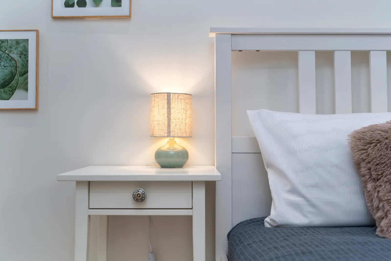 A small bedside lamp lit on a white nightstand.