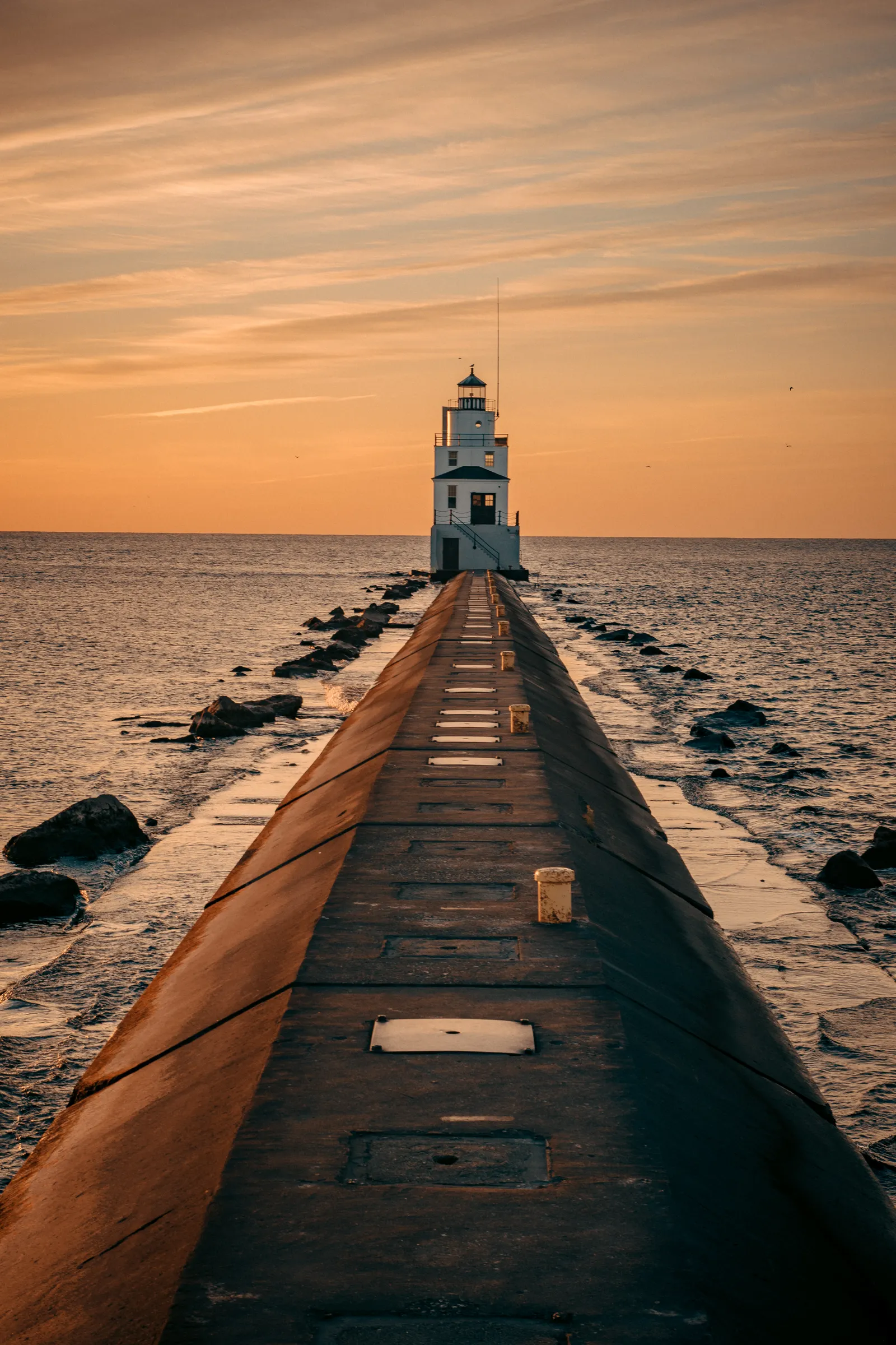 A white lighthouse at the end of a pier at sunset.