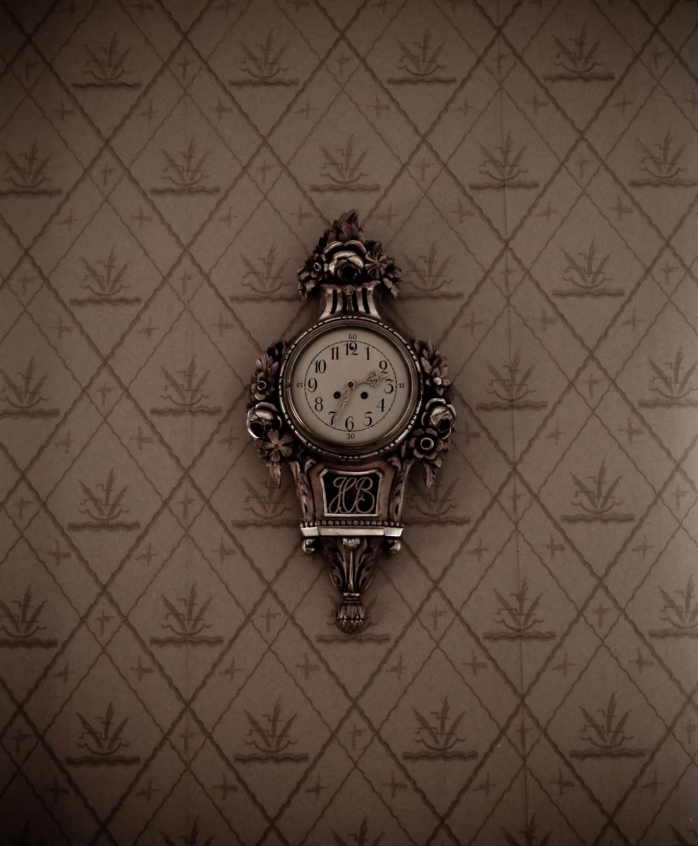 An ornate silver wall clock on patterned wallpaper.